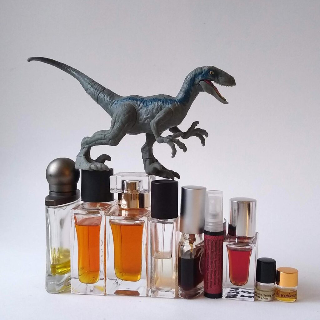 a toy dinosaur on top of a row of small perfume bottles.