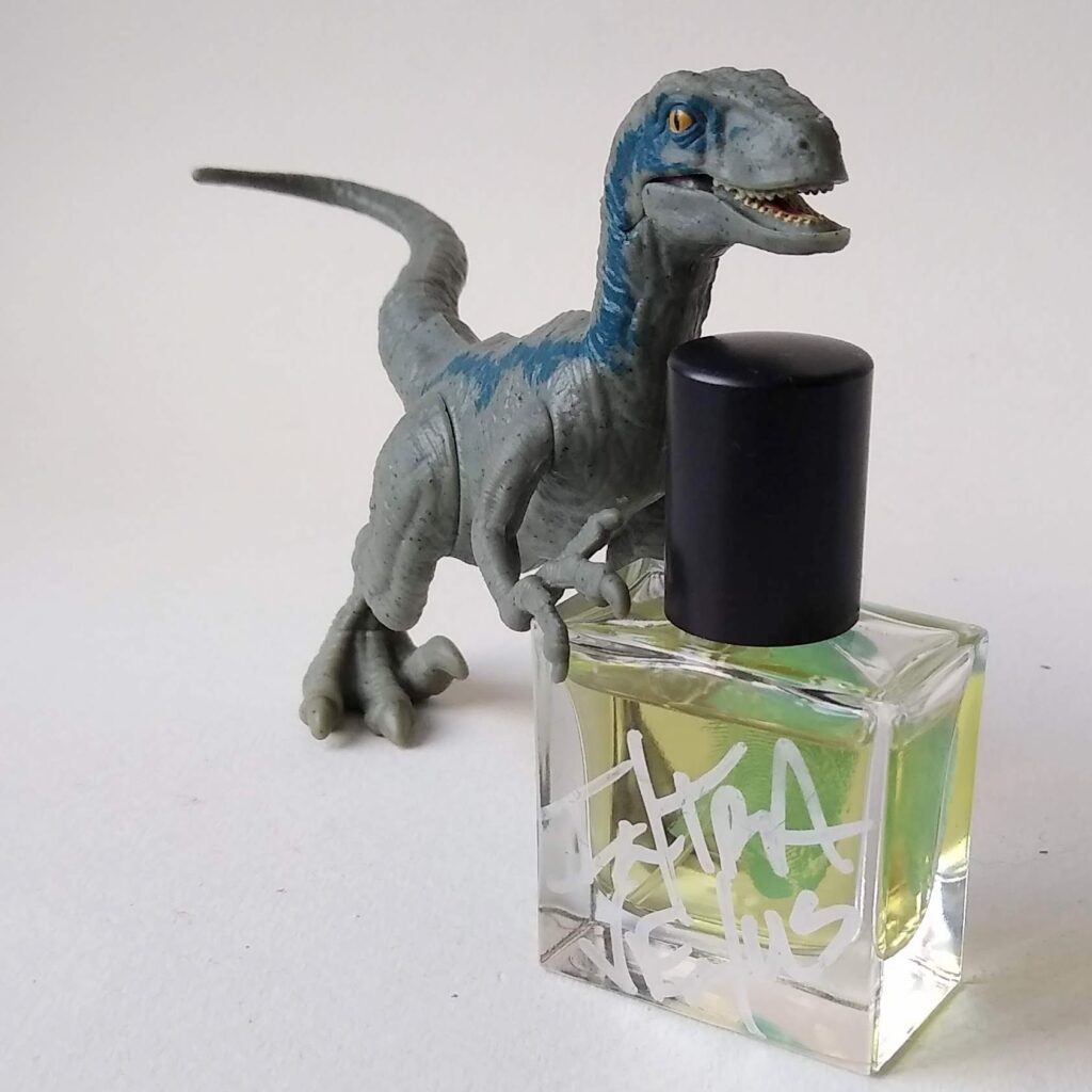 a blue and grey plastic toy velociraptor holds a glass bottle with silver handwriting on it: intra venus