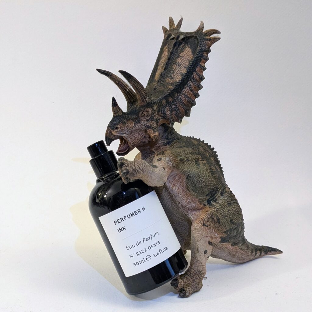 A plastic toy pentaceratops holding 50ml black glass bottle with a white label.