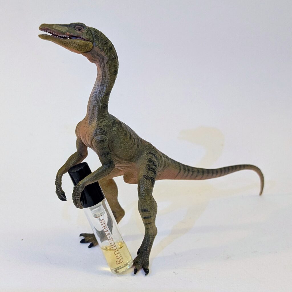 A plastic Compsognathus dinosaur toy, resting a small glass sample vial of perfume against its foot.
