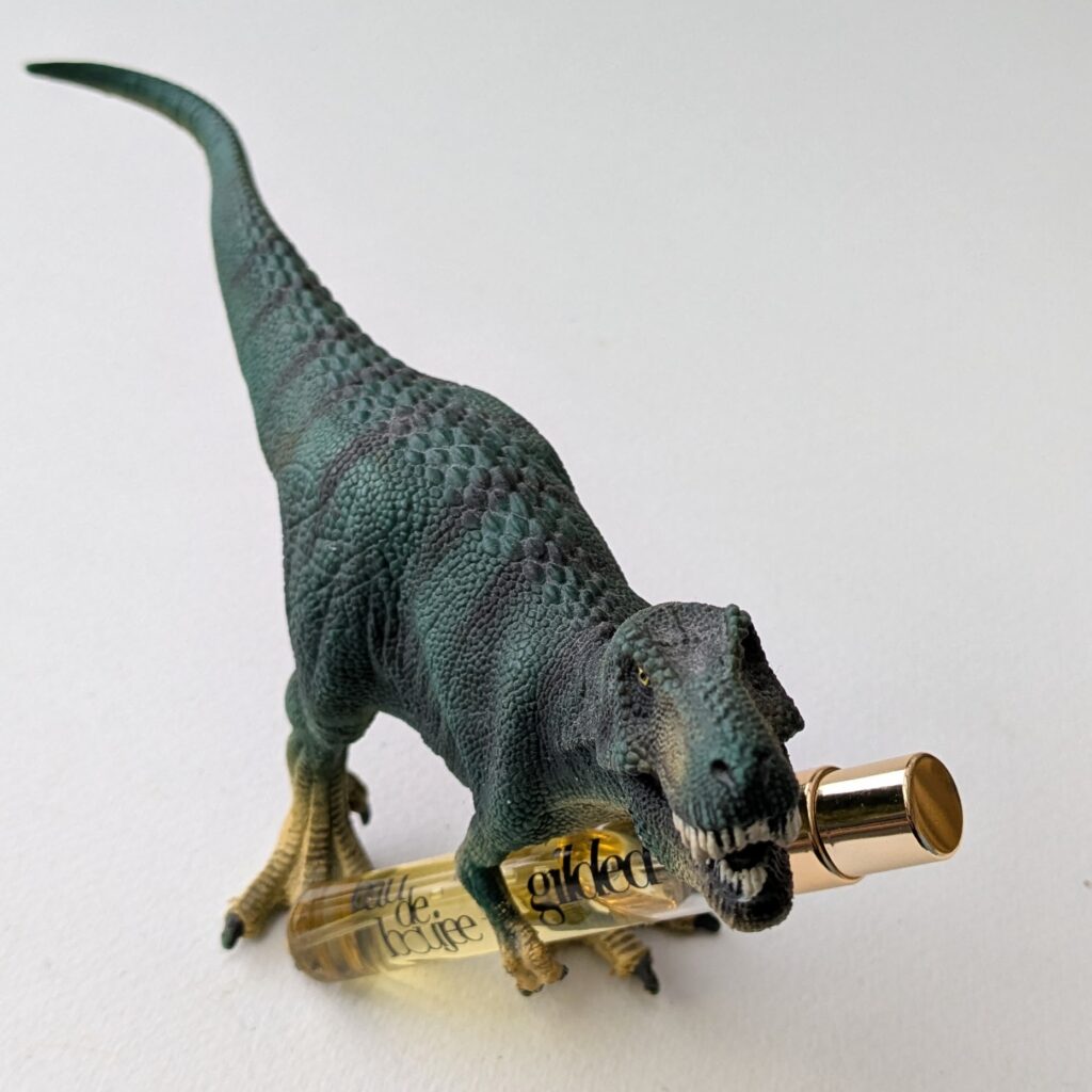 a plastic model of a juvenile t-rex, clutching a travel spray of Gilded